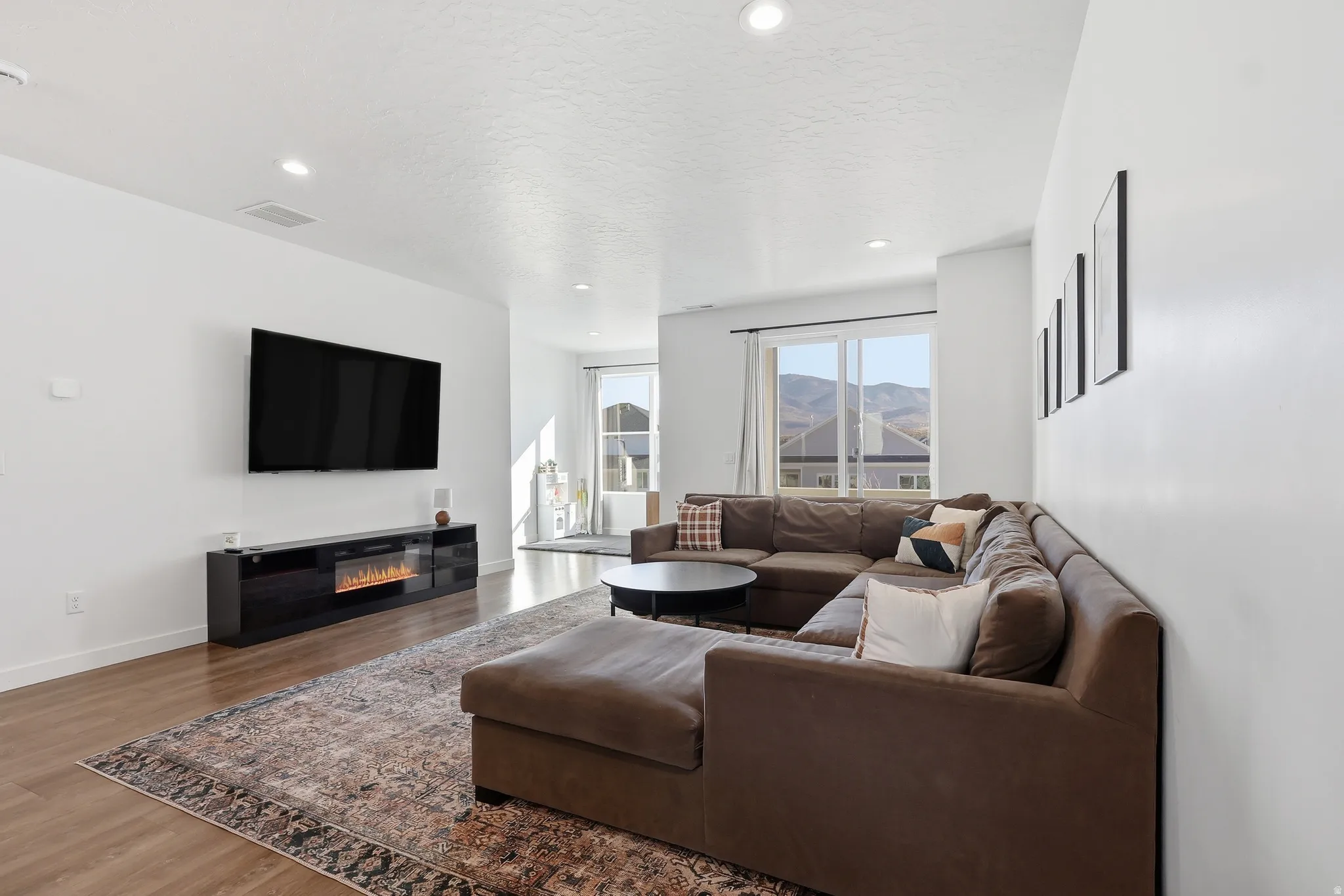 Living room with a glass covered fireplace, wood finished floors, recessed lighting, and a textured ceiling
