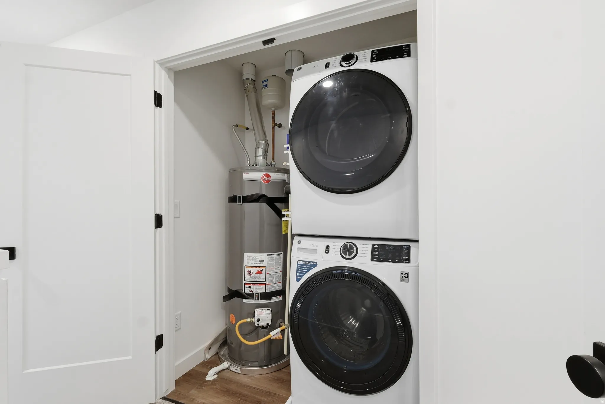 Laundry room featuring water heater, wood finished floors, and stacked washer / dryer