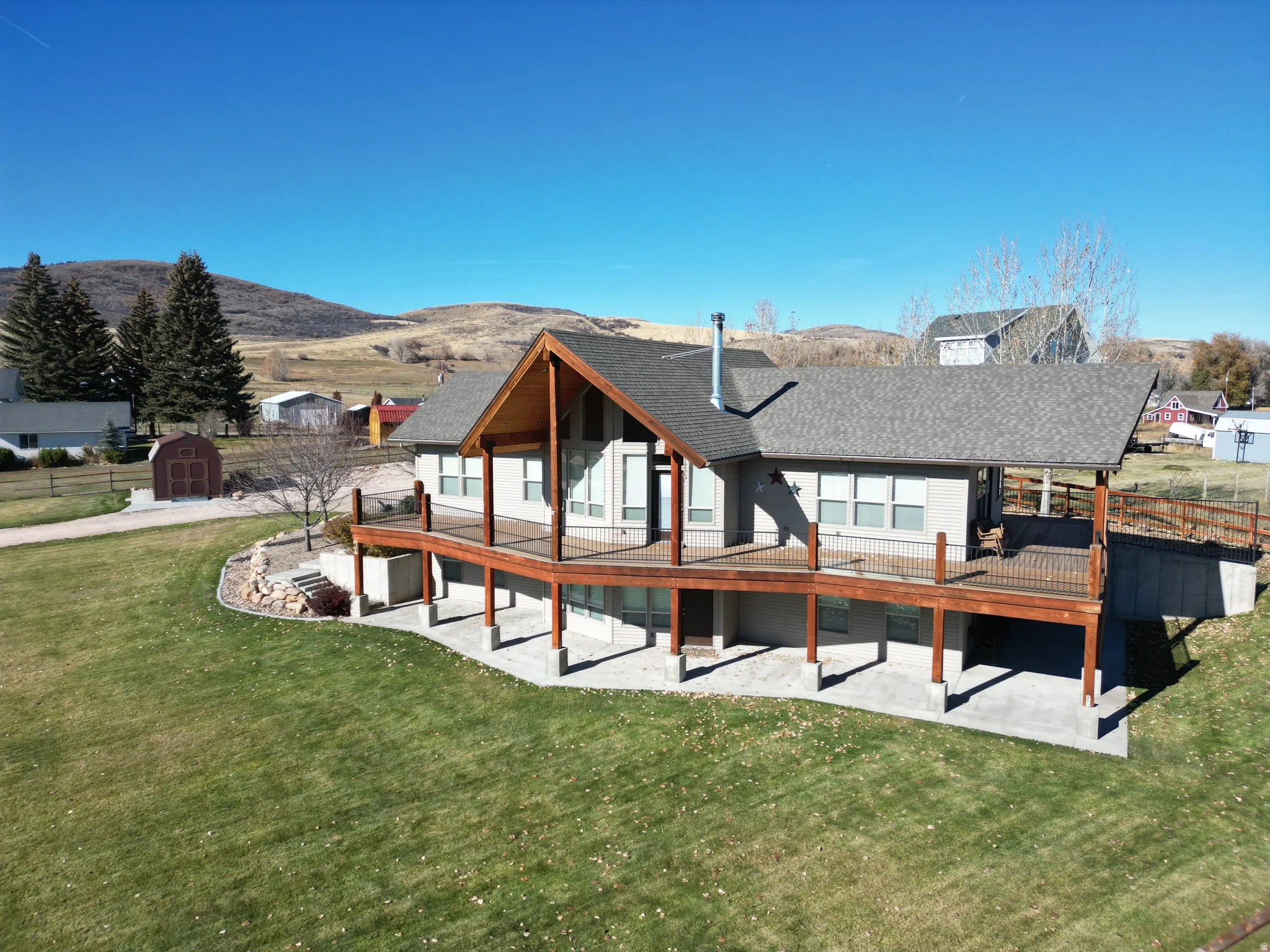 Back of house with a lawn, a deck with mountain view, a patio area, and roof with shingles