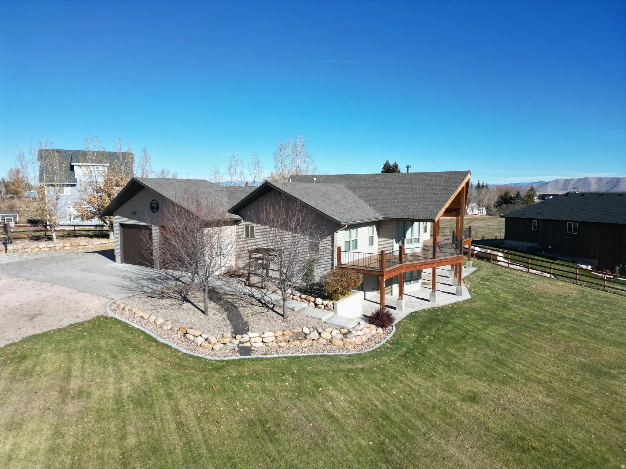 Rear view of house featuring stone siding, a wooden deck, driveway, an attached garage, and roof with shingles