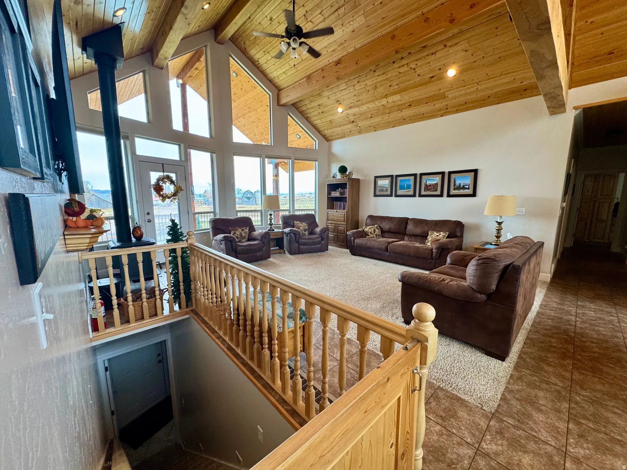 Carpeted living area with high vaulted ceiling, a wooden ceiling with exposed beams, ceiling fan, tile patterned floors, and a wood stove