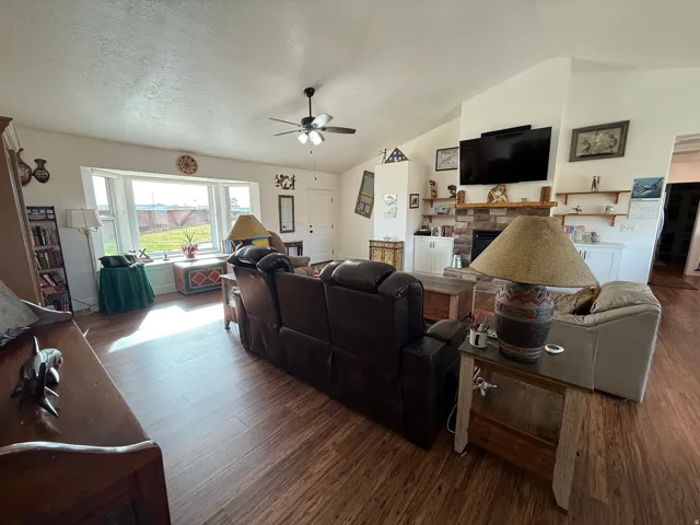 Living room featuring lofted ceiling, wood finished floors, a fireplace, a textured ceiling, and ceiling fan