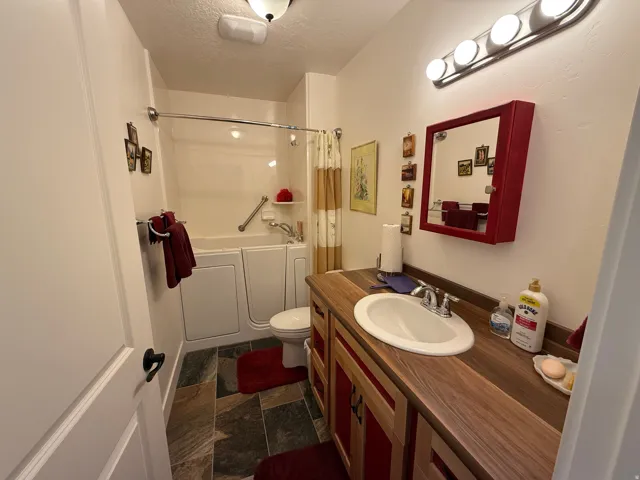 Bathroom with a textured ceiling, vanity, dark stone finish flooring, and shower / tub combo with curtain