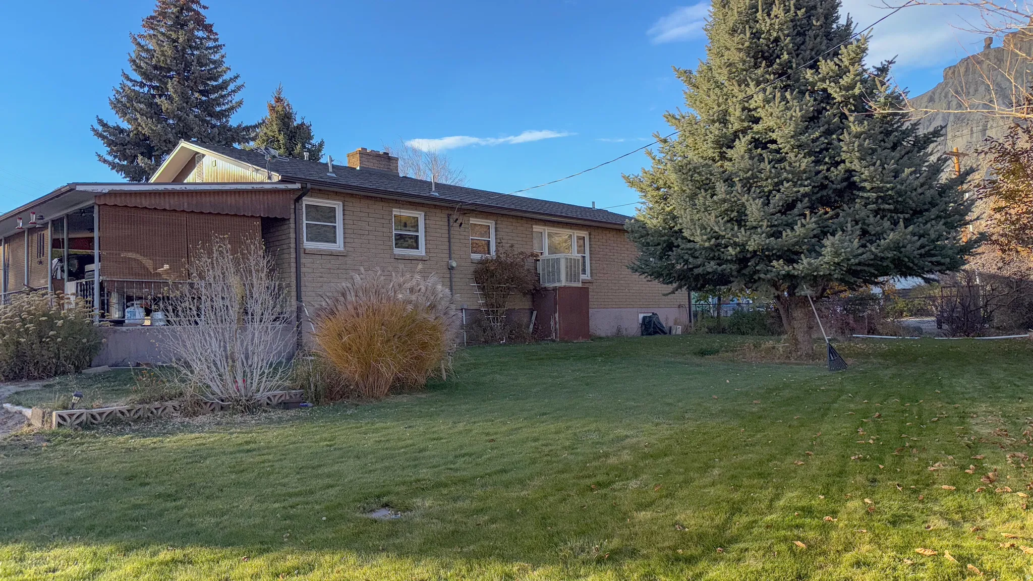 Rear view of property featuring a yard, a chimney, brick siding, and a sunroom