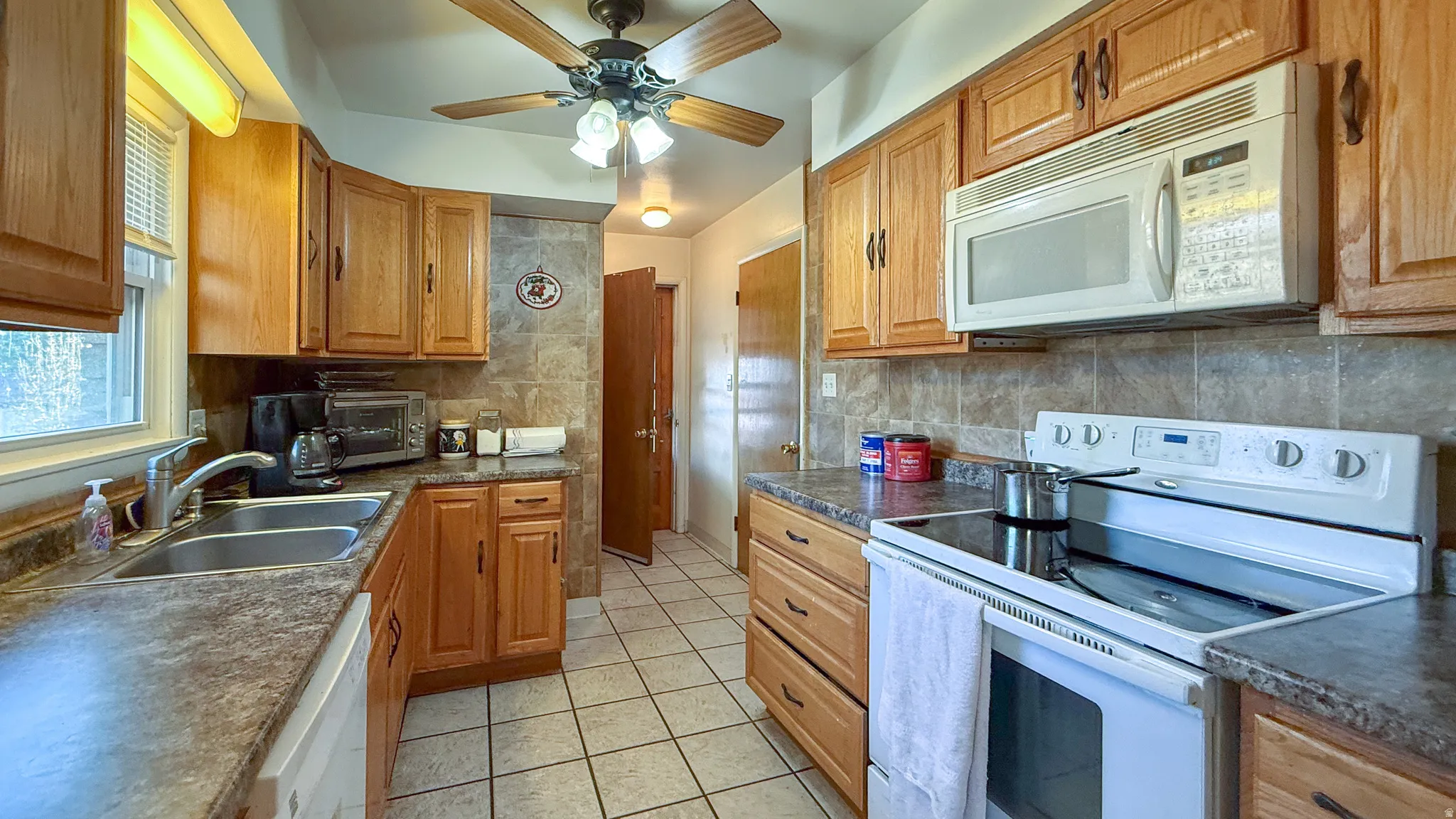 Kitchen with white appliances, dark countertops, light tile patterned floors, and a ceiling fan