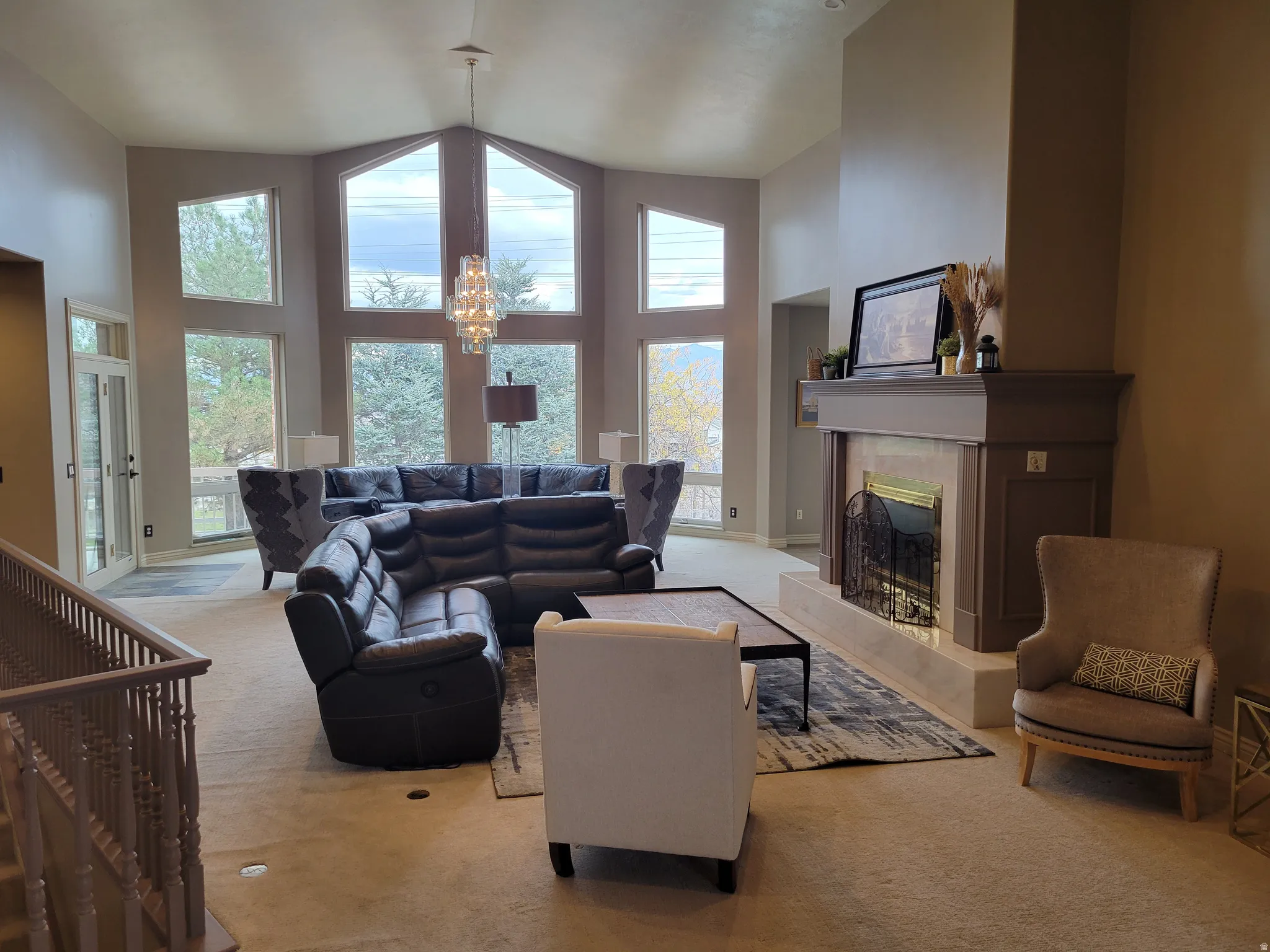 Carpeted living area featuring high vaulted ceiling, plenty of natural light, a fireplace, and a chandelier