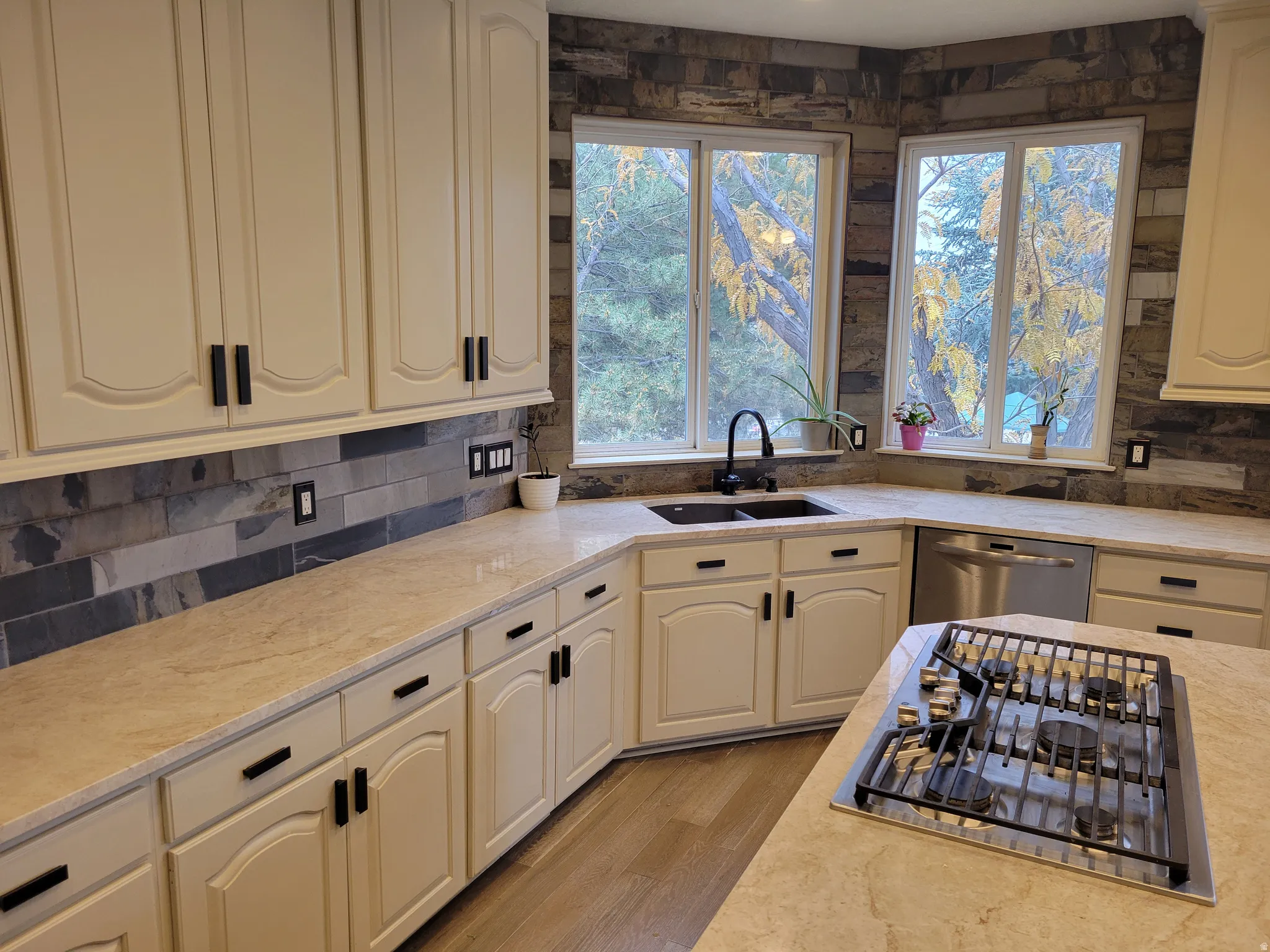 Kitchen with light stone counters, appliances with stainless steel finishes, wood finished floors, and decorative backsplash