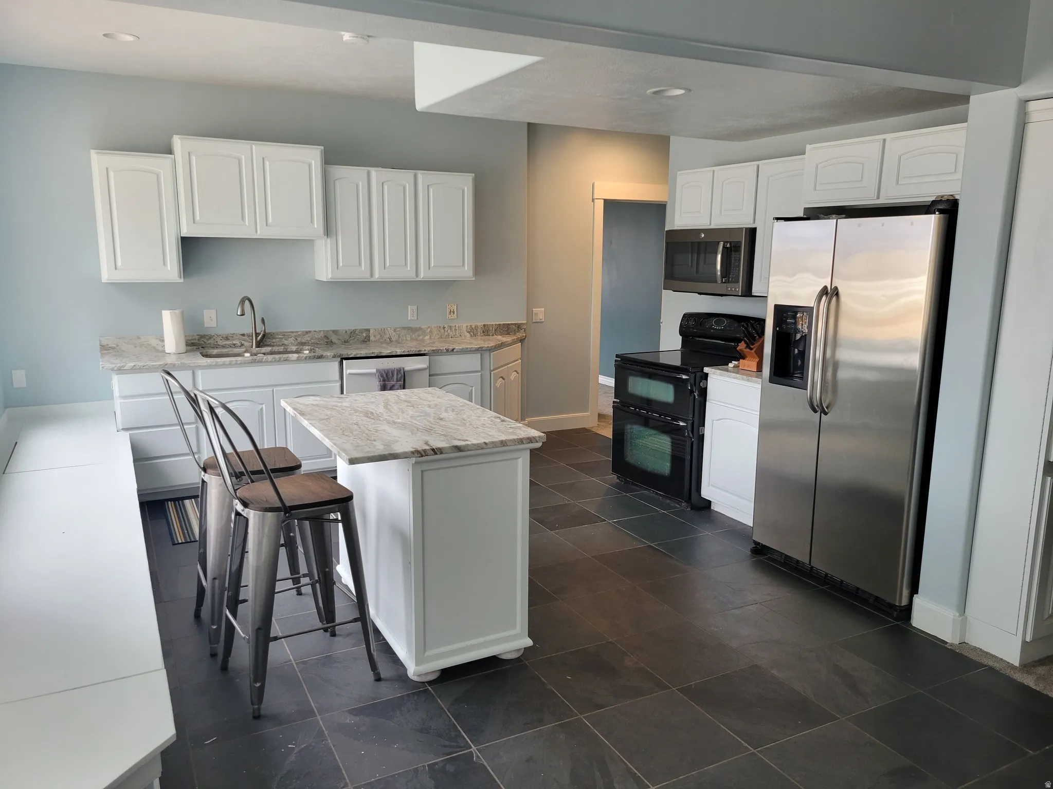 Kitchen featuring white cabinetry, appliances with stainless steel finishes, a kitchen breakfast bar, a center island, and light stone countertops
