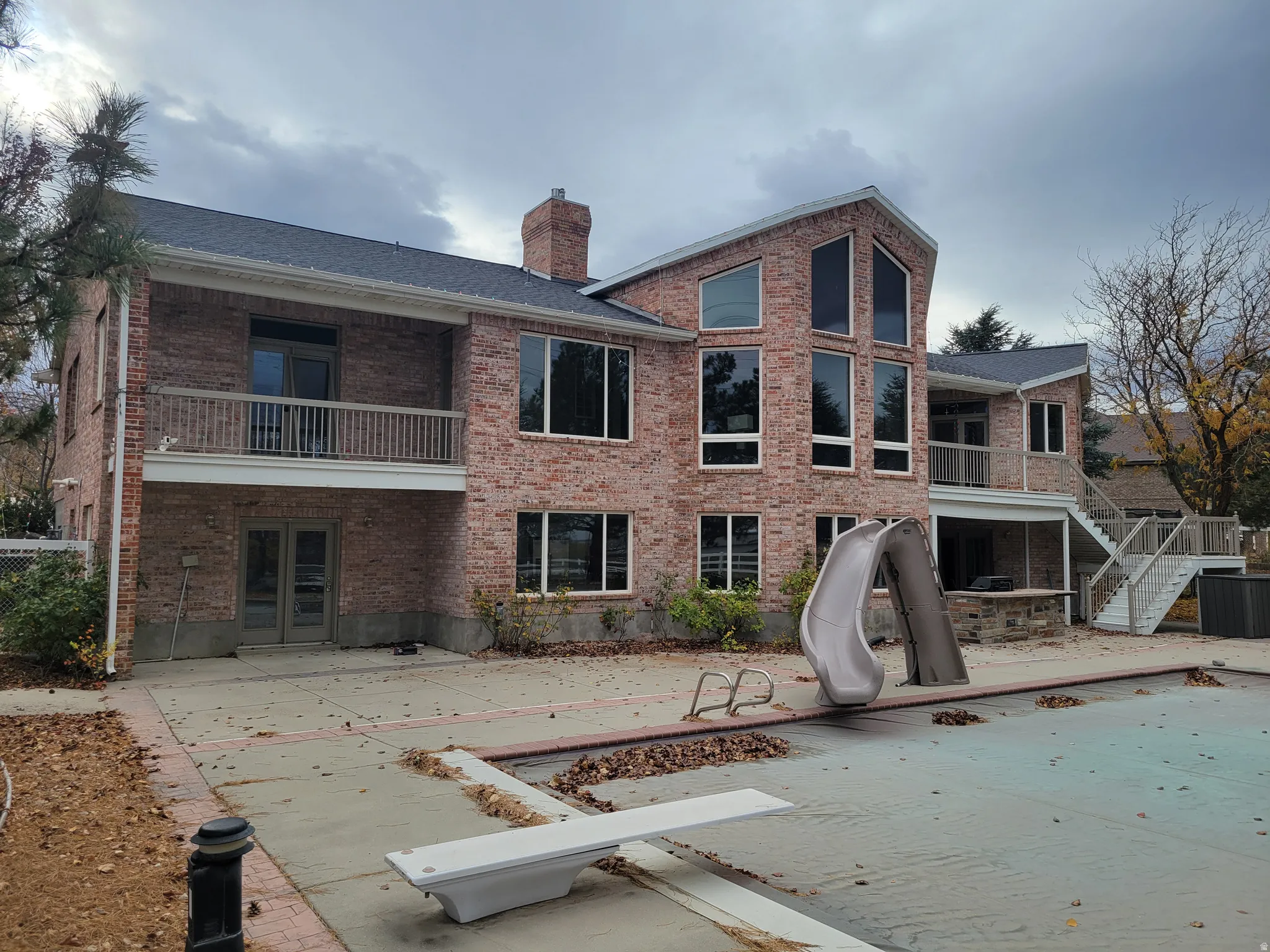 Rear view of property featuring stairway, brick siding, a covered pool, and a balcony