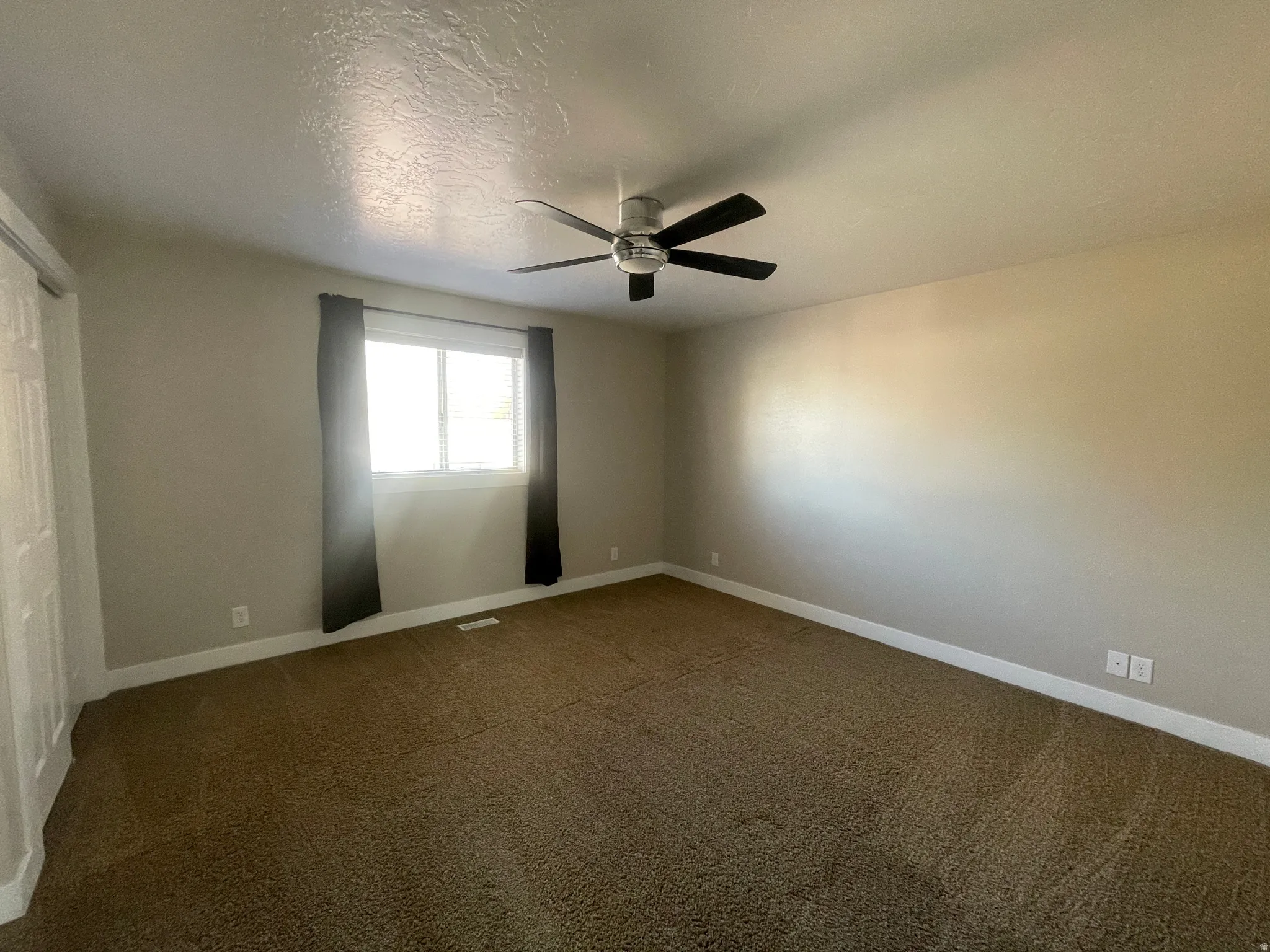 Empty room with a textured ceiling, carpet floors, and a ceiling fan