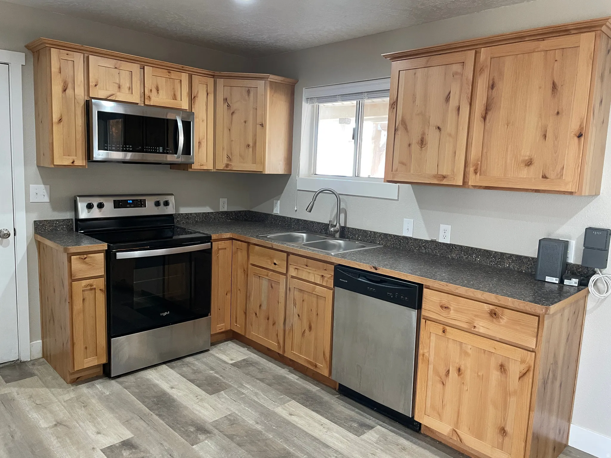 Kitchen featuring appliances with stainless steel finishes, dark countertops, light wood finished floors, light brown cabinets, and a textured ceiling