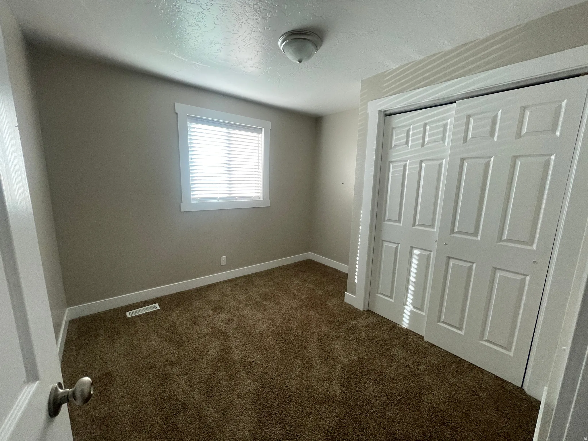 Unfurnished bedroom with dark carpet, a textured ceiling, and a closet