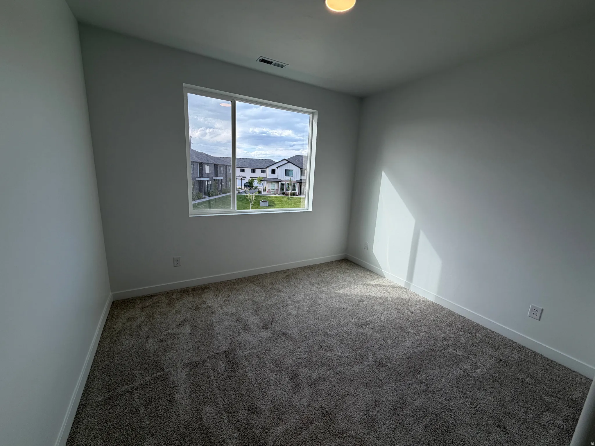 Spacious room featuring neutral carpeting, white walls, a large window, white trim, and a recessed ceiling light