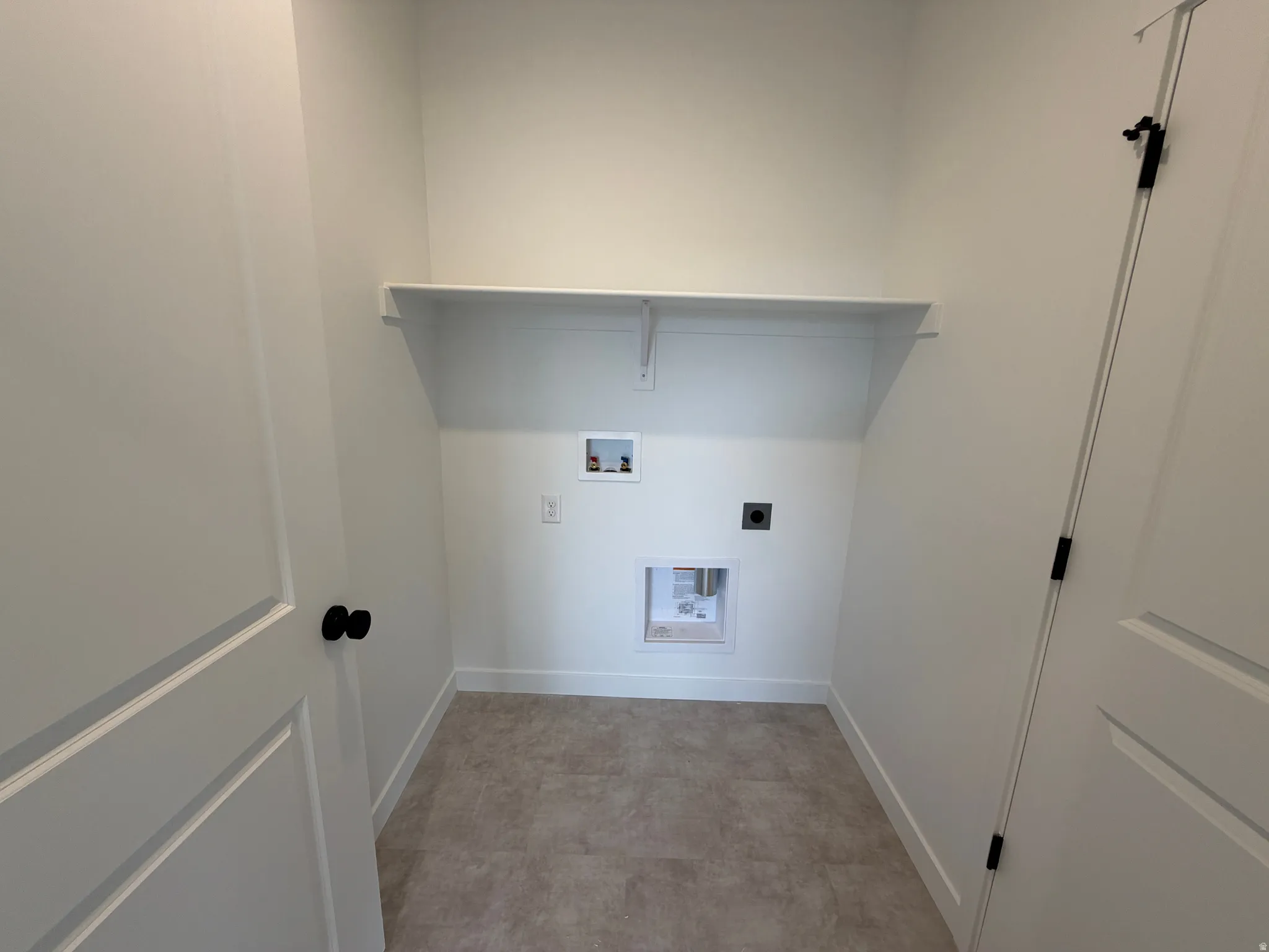 Dedicated laundry area featuring a built-in shelf, plumbing hookups, electrical outlet, and neutral-toned flooring
