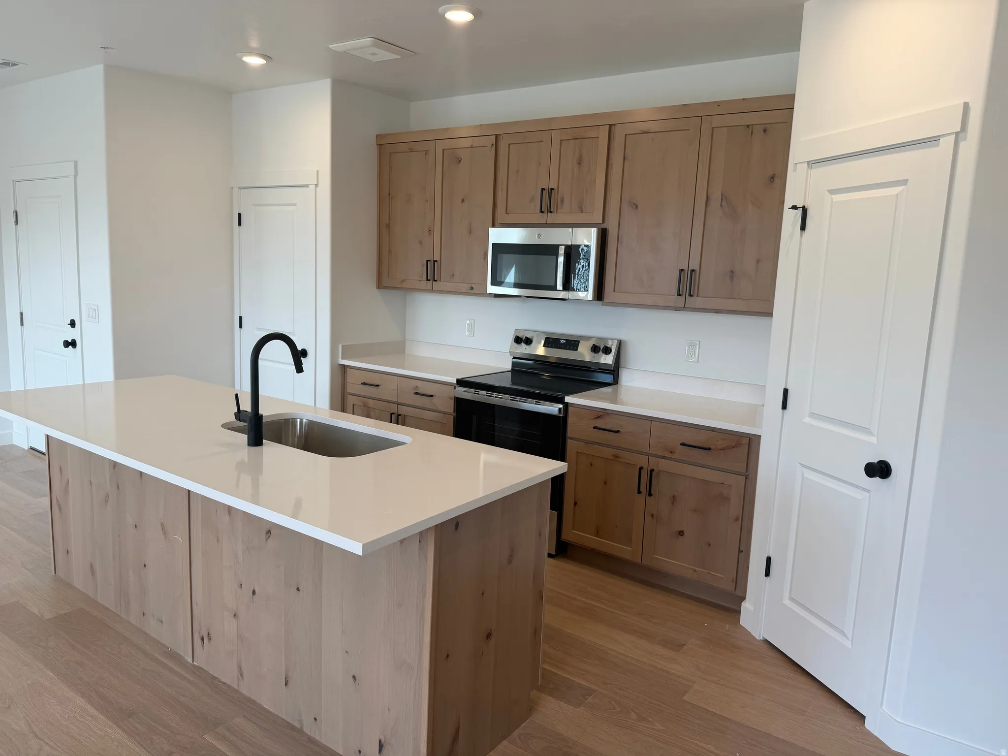 Kitchen featuring light wood-finish cabinetry, white solid surface countertops, and stainless steel appliances