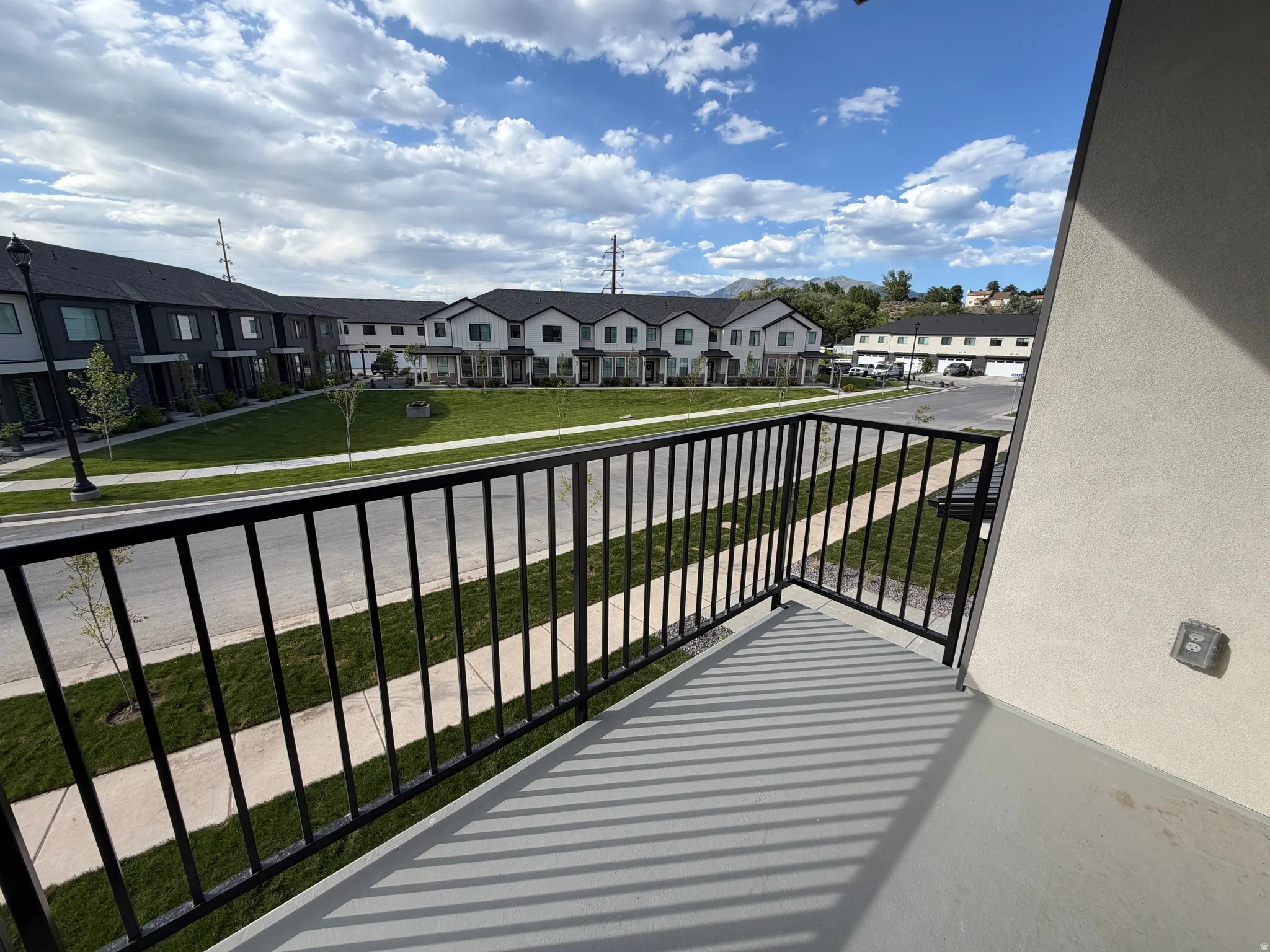 Private balcony with black metal railing, overlooking a landscaped common area with green lawns and sidewalks