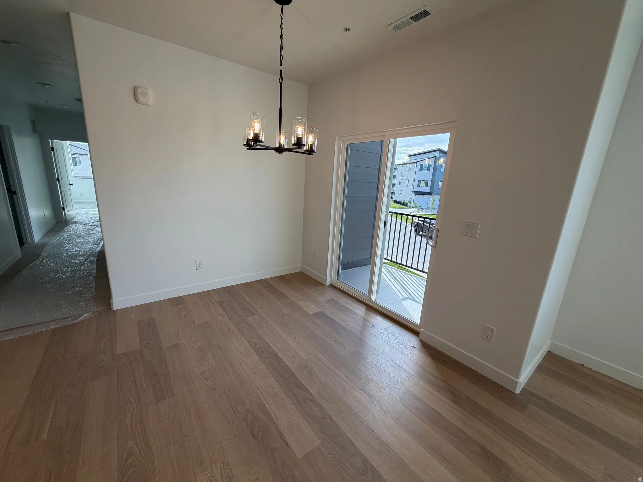 Open concept room featuring wood-finish flooring, white walls, and a contemporary black chandelier with clear glass shades