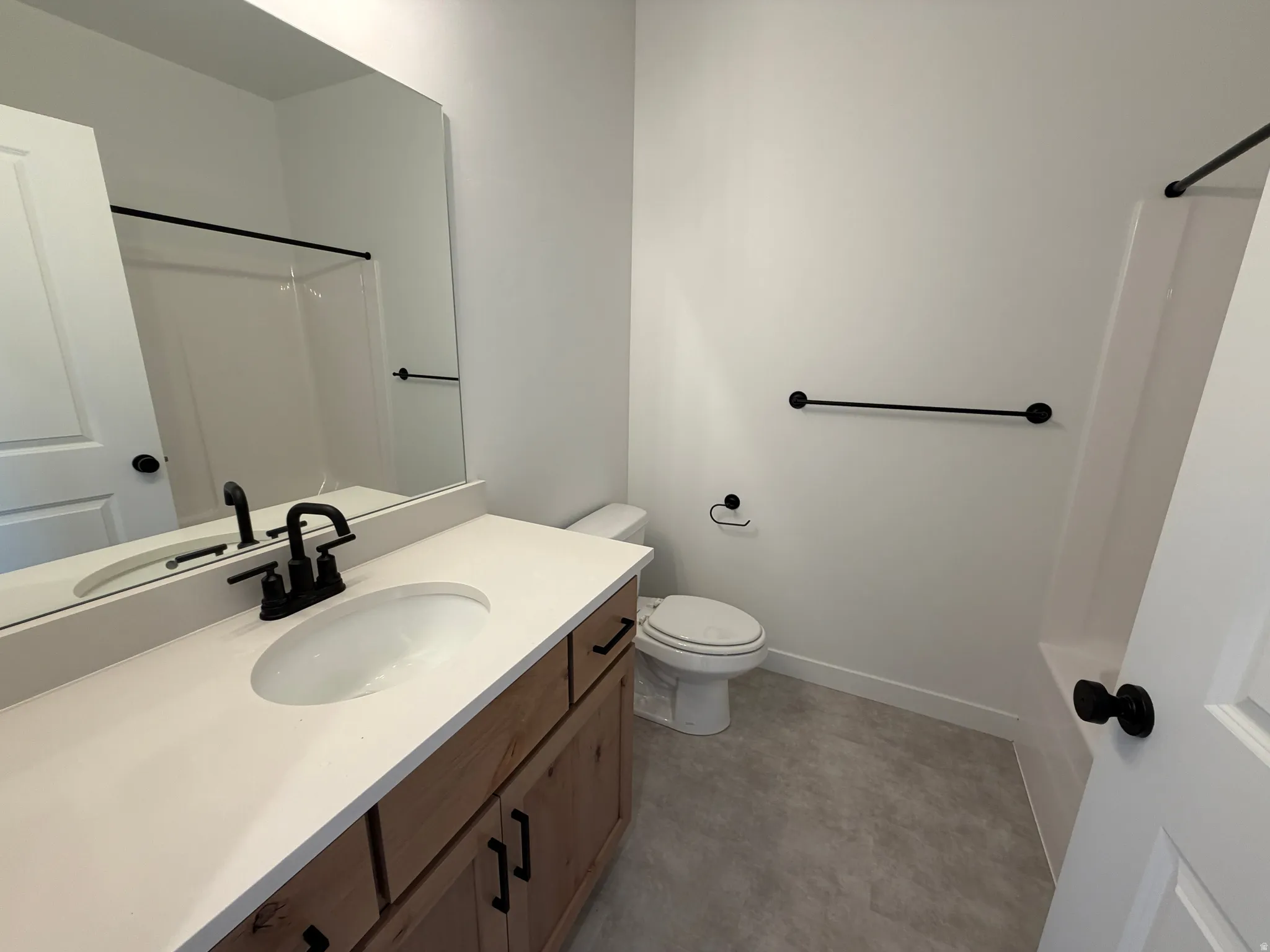 Bathroom featuring a light wood-finish vanity with a white countertop and oval sink, matte black faucet, and coordinating hardware