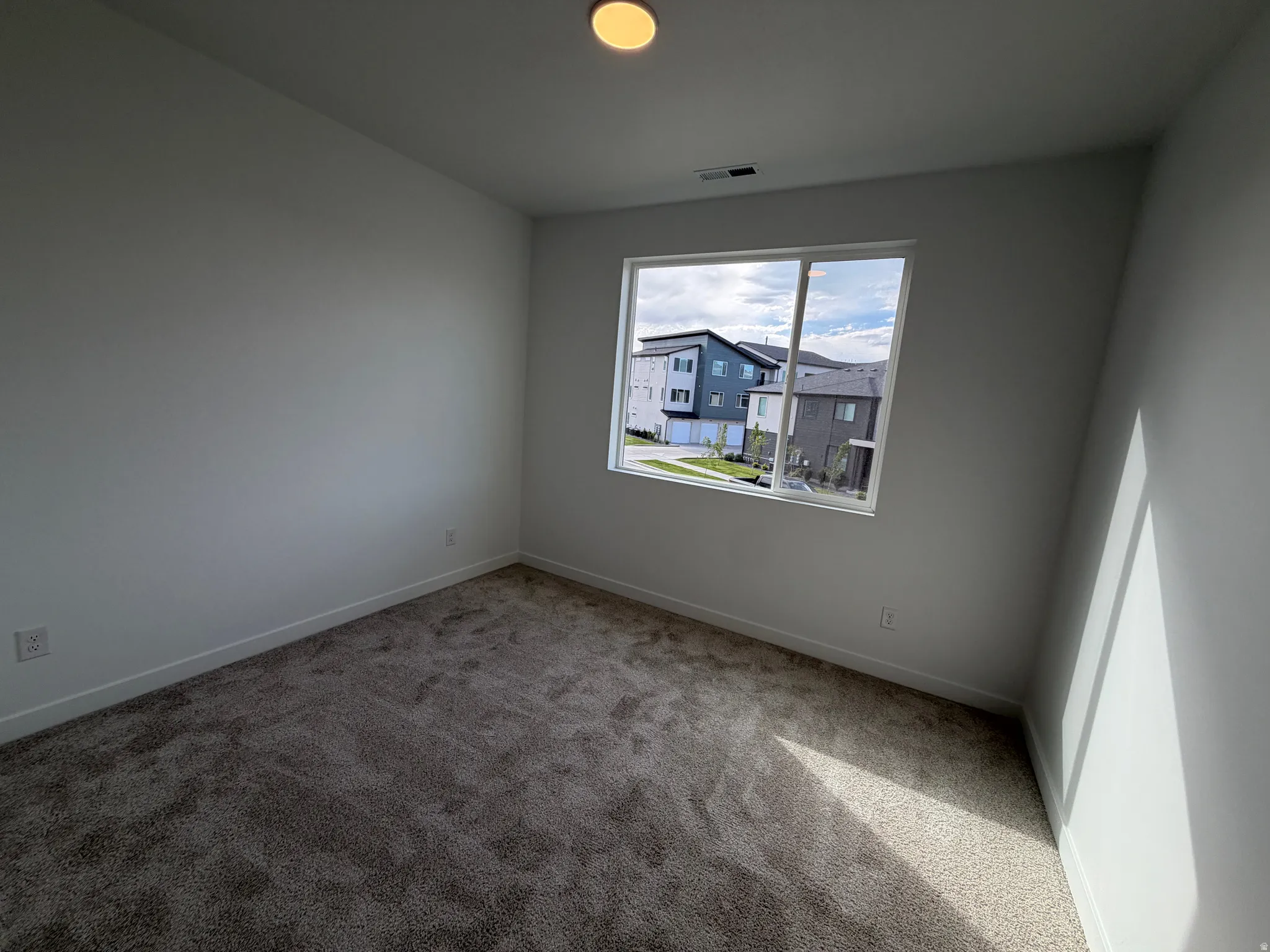 Square room featuring plush carpet flooring, white baseboards, and a single window offering exterior surroundings