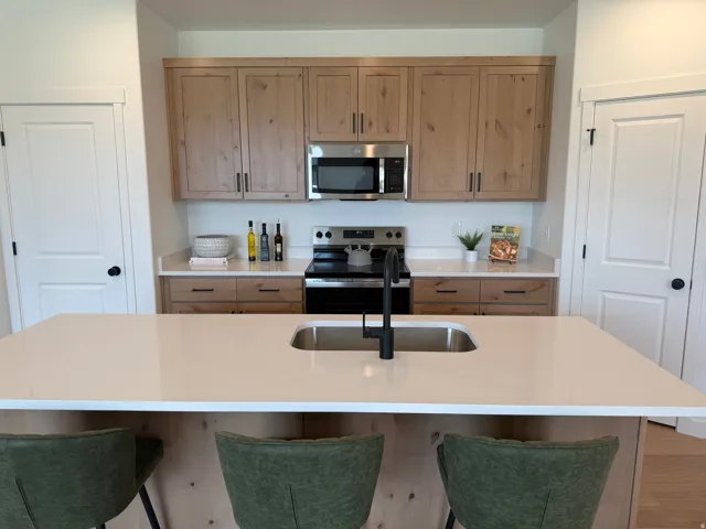 Kitchen featuring light wood-finish cabinetry, stainless steel appliances, white countertops, a kitchen island with an undermount sink, and a matte black faucet