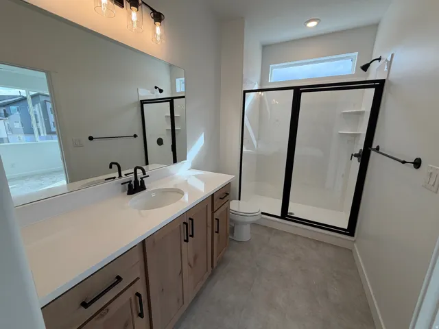Modern bathroom featuring a wood-finish vanity with a white countertop and undermount sink, complemented by black hardware and a frameless mirror