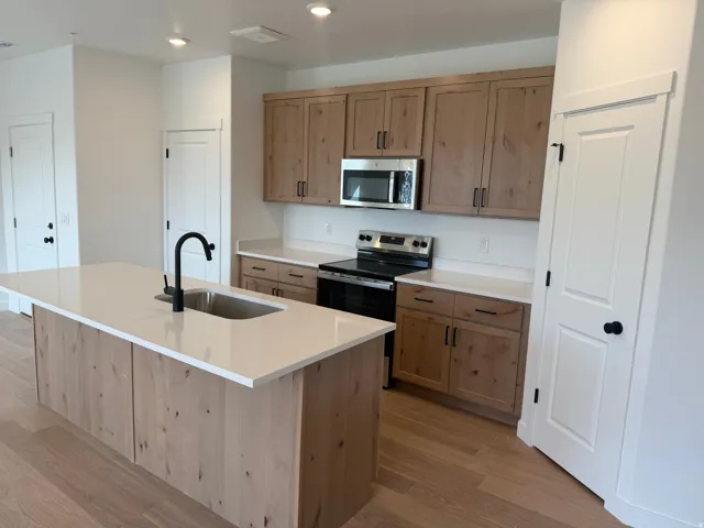 Kitchen featuring light wood-finish cabinetry, white solid surface countertops, and stainless steel appliances
