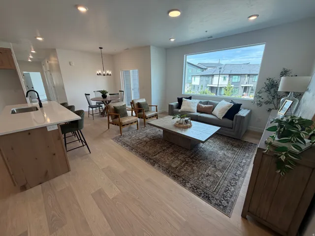 Open-concept living space with light wood-finish flooring, recessed lighting, a kitchen island with stone countertops, and a large picture window