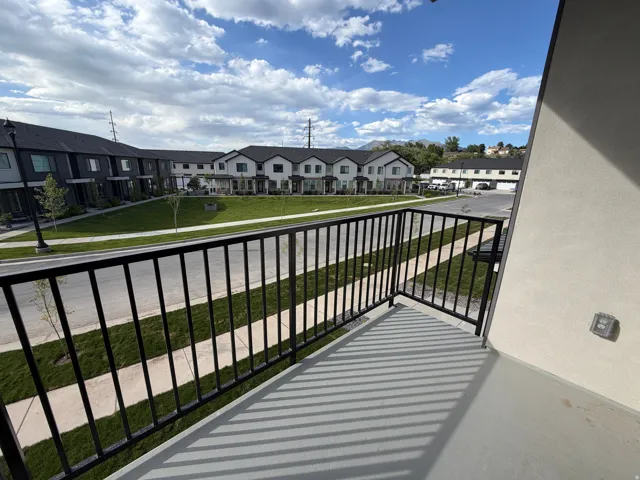 Private balcony with black metal railing, overlooking a landscaped common area with green lawns and sidewalks