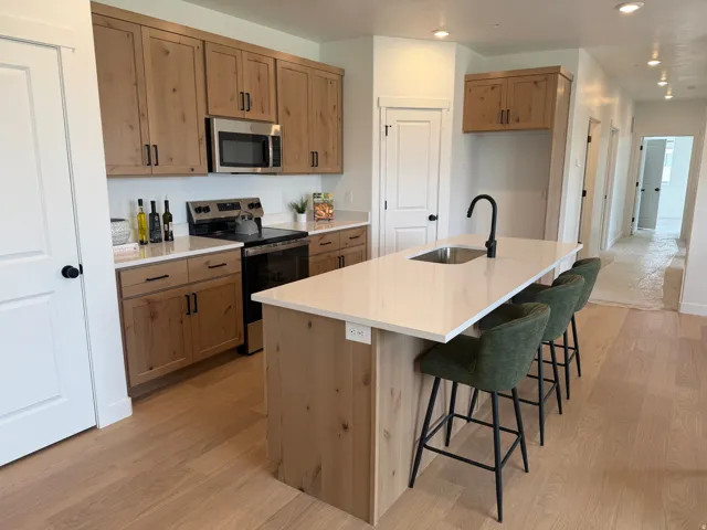 Kitchen featuring wood-finish cabinetry, stainless steel appliances, light-toned countertops, a kitchen island with seating space, and wood-finish flooring