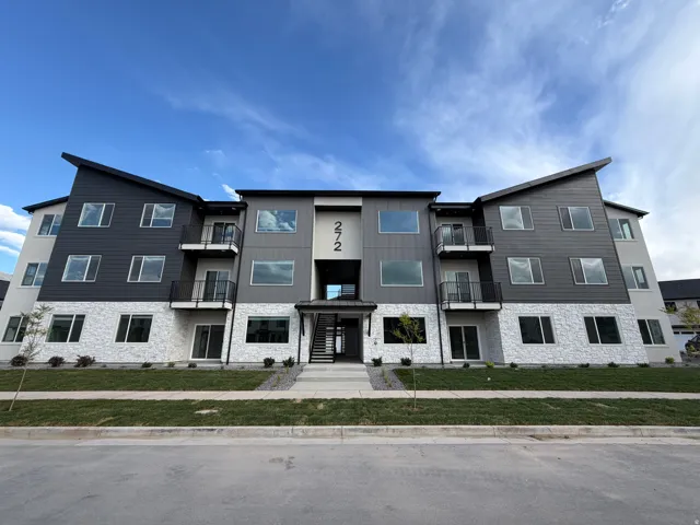 Modern multi-story building featuring a distinctive roofline, a mix of light-colored stone veneer and dark horizontal siding, multiple windows, and private balconies with dark railings