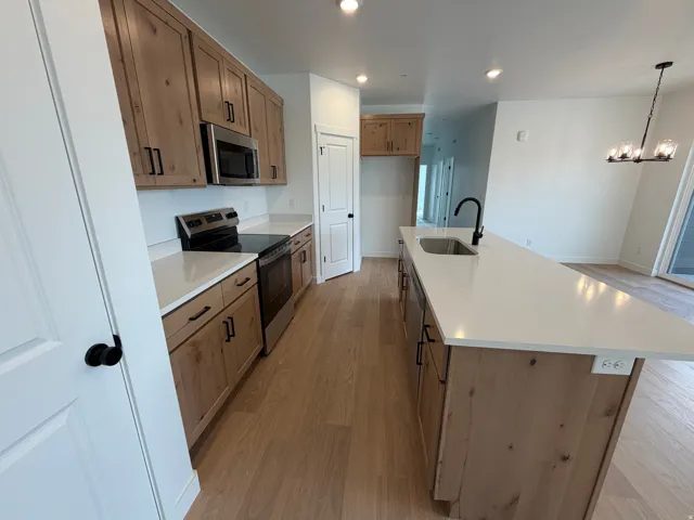 Contemporary kitchen featuring light wood-finish cabinetry, stainless steel appliances, white countertops, and wood-finish flooring