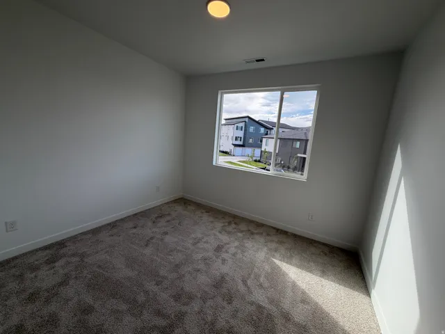 Square room featuring plush carpet flooring, white baseboards, and a single window offering exterior surroundings