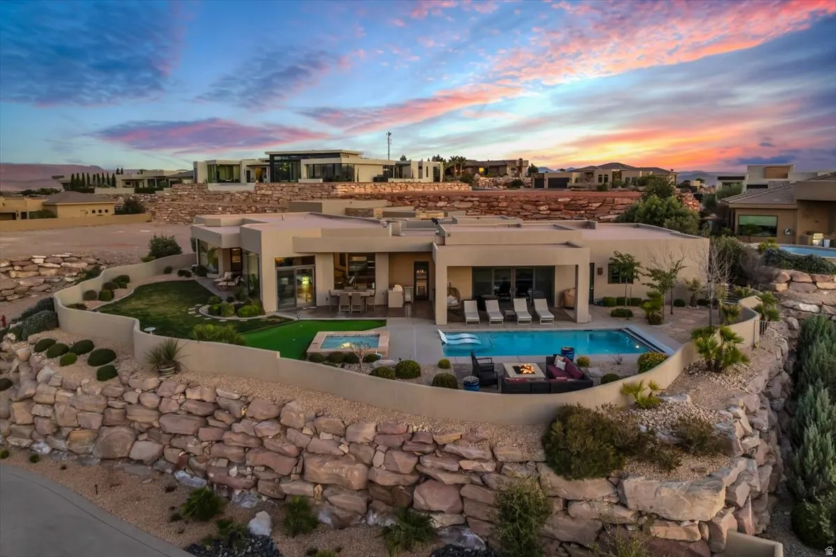 Rear view of property with an outdoor pool, a patio, an in-ground hot tub, stucco siding, and an outdoor fire pit