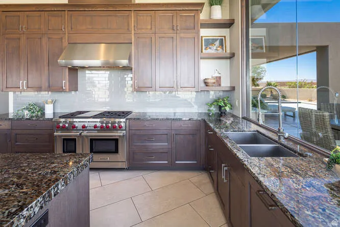 Kitchen featuring double oven range, range hood, dark stone countertops, decorative backsplash, and open shelves