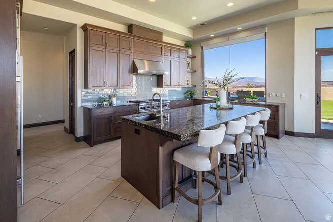 Kitchen featuring backsplash, a kitchen island with sink, dark stone countertops, a kitchen bar, and open shelves