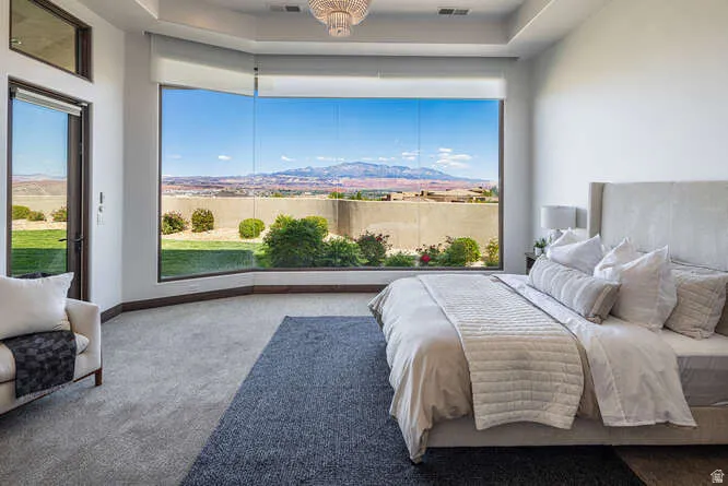 Carpeted bedroom with a tray ceiling, multiple windows, and access to exterior
