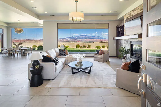 Living room featuring a chandelier, a stone fireplace, light tile patterned floors, a raised ceiling, and recessed lighting