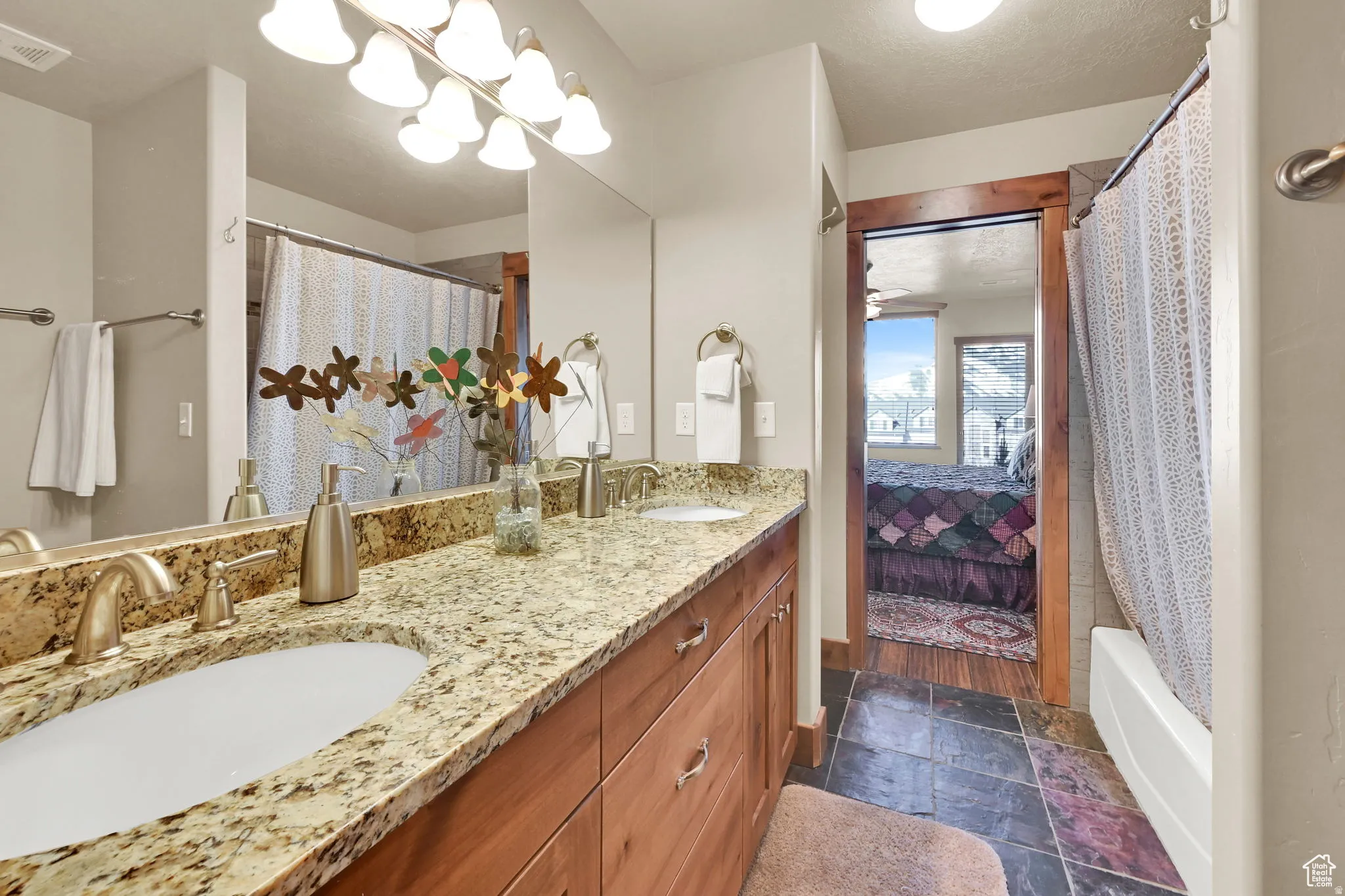 Ensuite bathroom featuring double vanity, shower / bath combo with shower curtain, and stone tile flooring