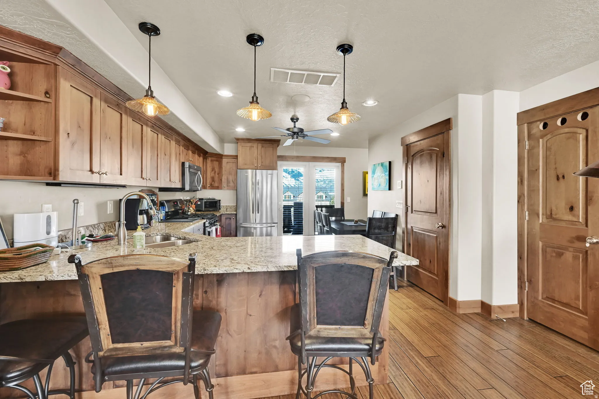 Kitchen featuring a peninsula, light stone counters, pendant lighting, brown cabinetry, and recessed lighting