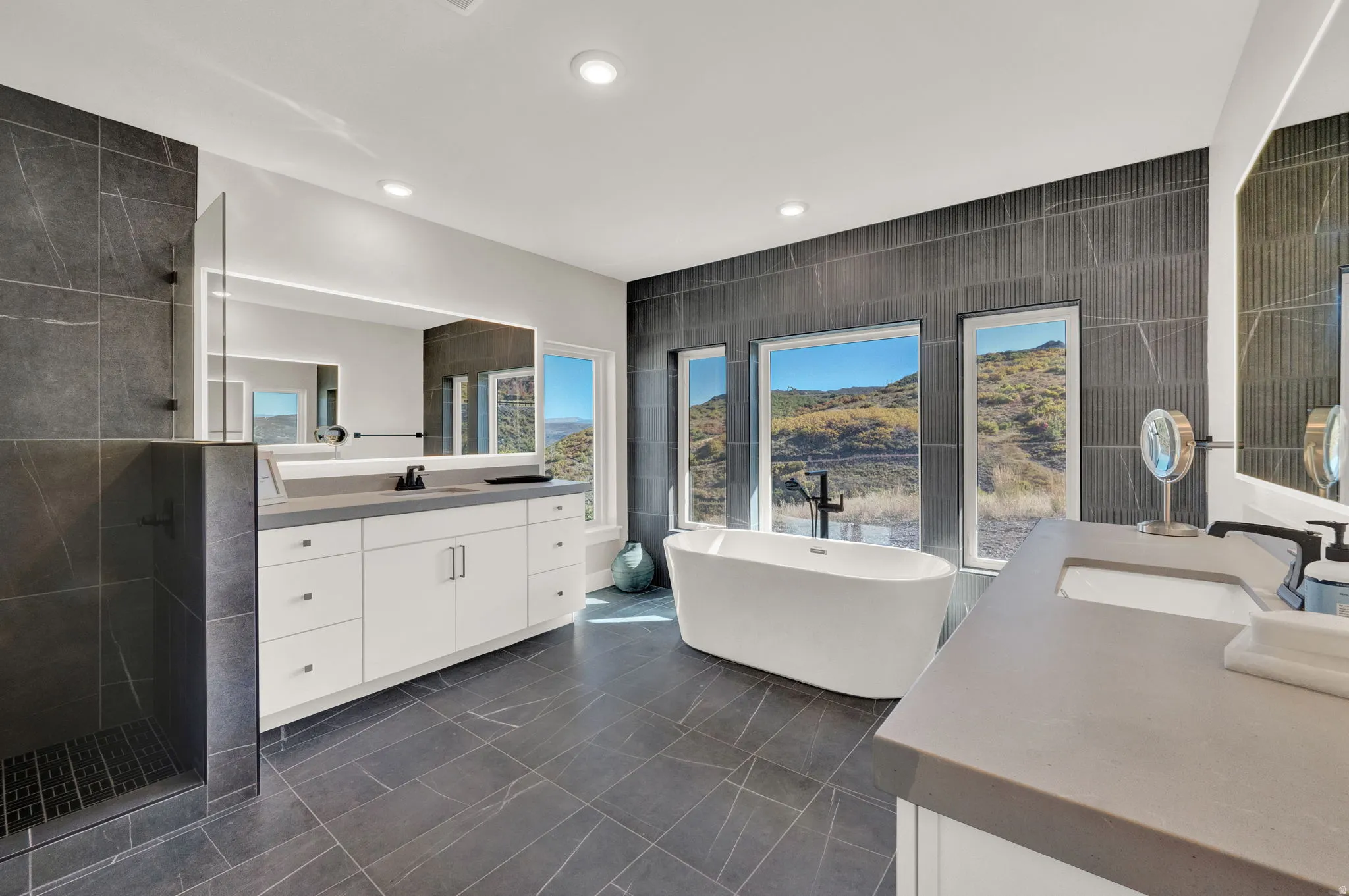Bathroom with tile walls, a freestanding tub, two vanities, a shower stall, and recessed lighting
