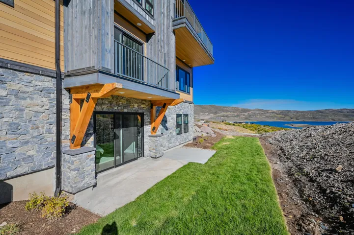 View of green lawn featuring a balcony, a water view, and a patio