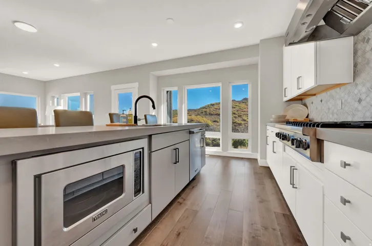 Kitchen with stainless steel appliances, white cabinets, wall chimney range hood, backsplash, and light wood finished floors