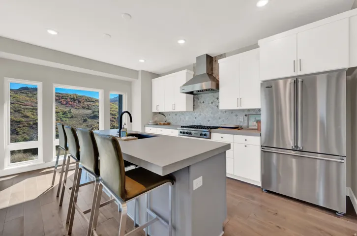 Kitchen featuring stainless steel appliances, decorative backsplash, light wood-type flooring, wall chimney exhaust hood, and a center island with sink