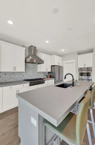 Kitchen featuring white cabinets, backsplash, a center island with sink, a kitchen breakfast bar, and recessed lighting