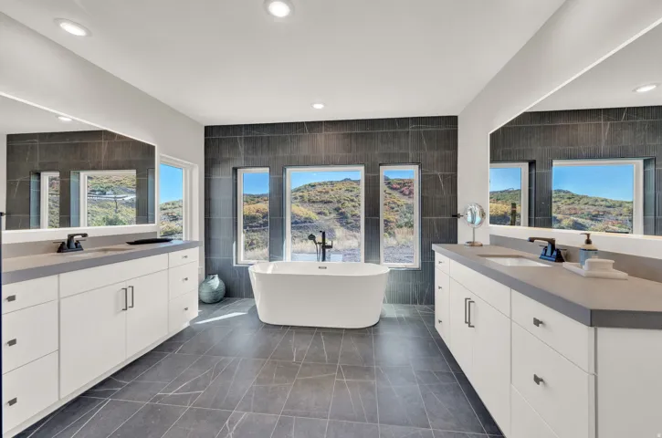 Bathroom with tile walls, two vanities, a freestanding tub, healthy amount of natural light, and recessed lighting