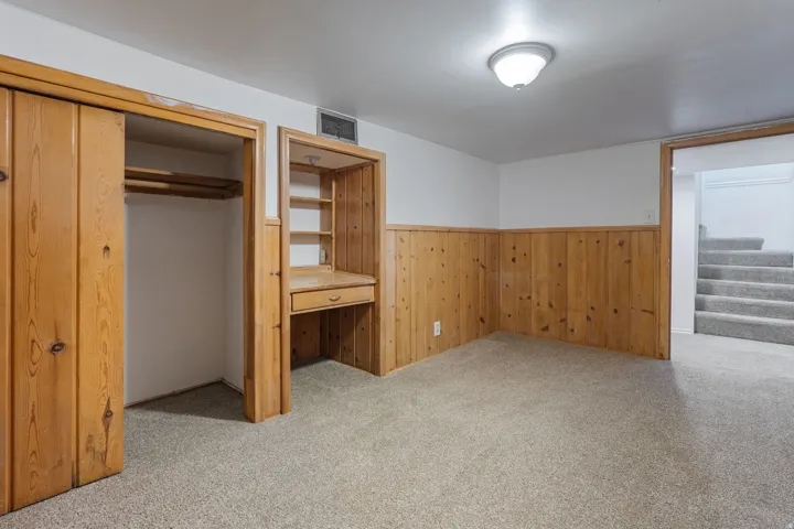 Unfurnished bedroom with light carpet, a closet, wooden walls, and built in study area