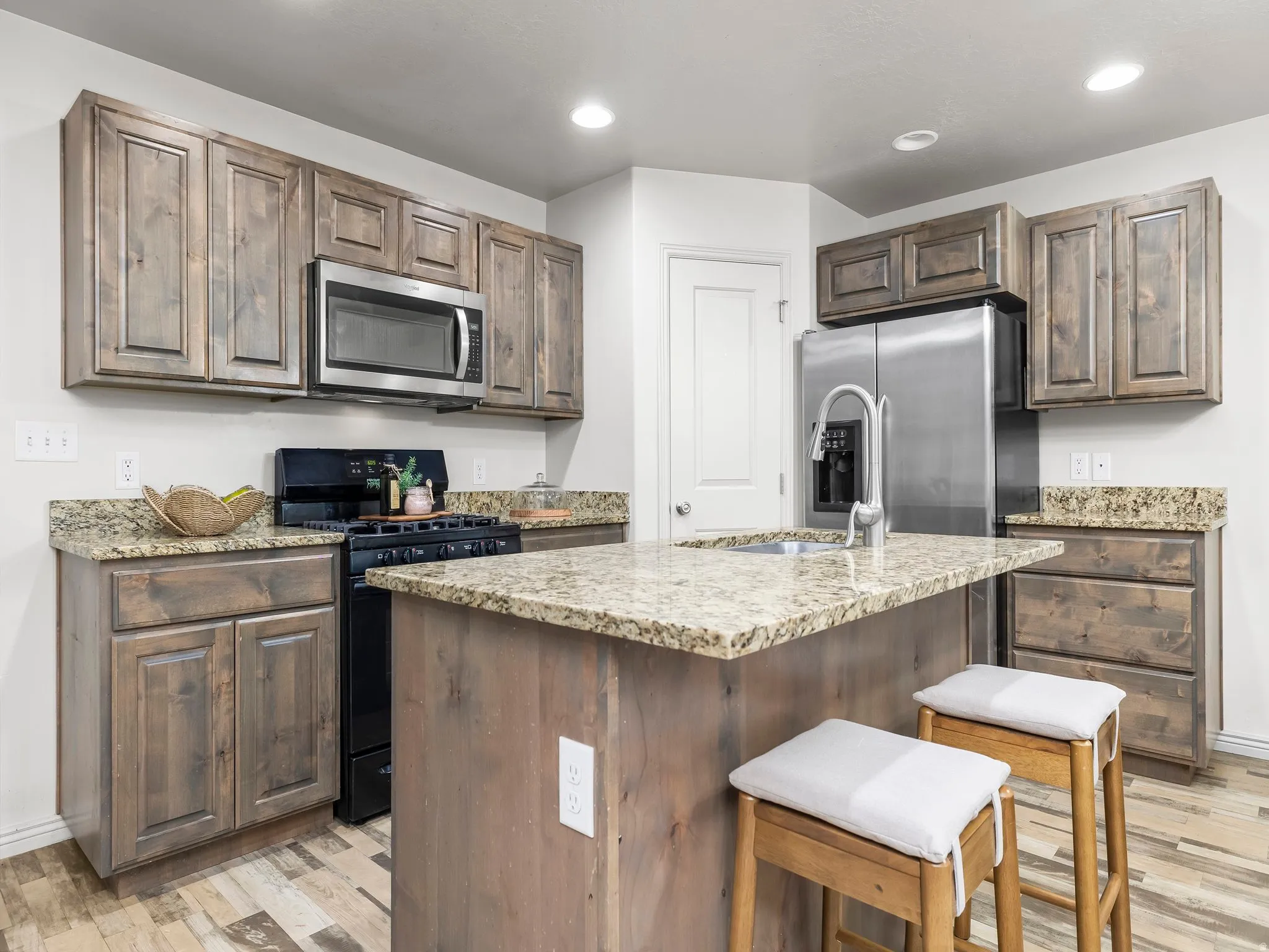 Kitchen with appliances with stainless steel finishes, an island with sink, light stone counters, light wood finished floors, and a breakfast bar area