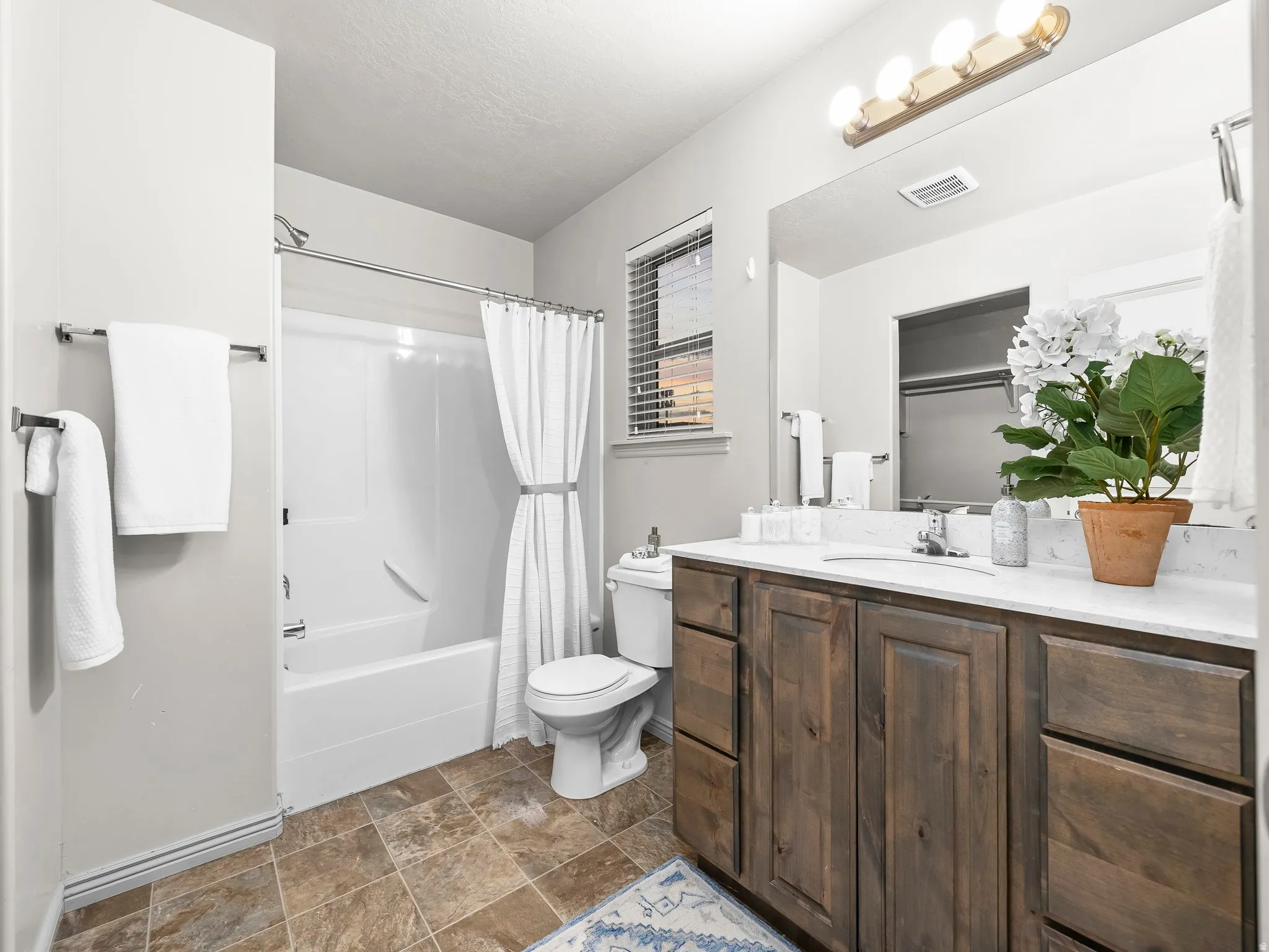 Bathroom featuring shower / bath combination with curtain, vanity, and stone finish flooring