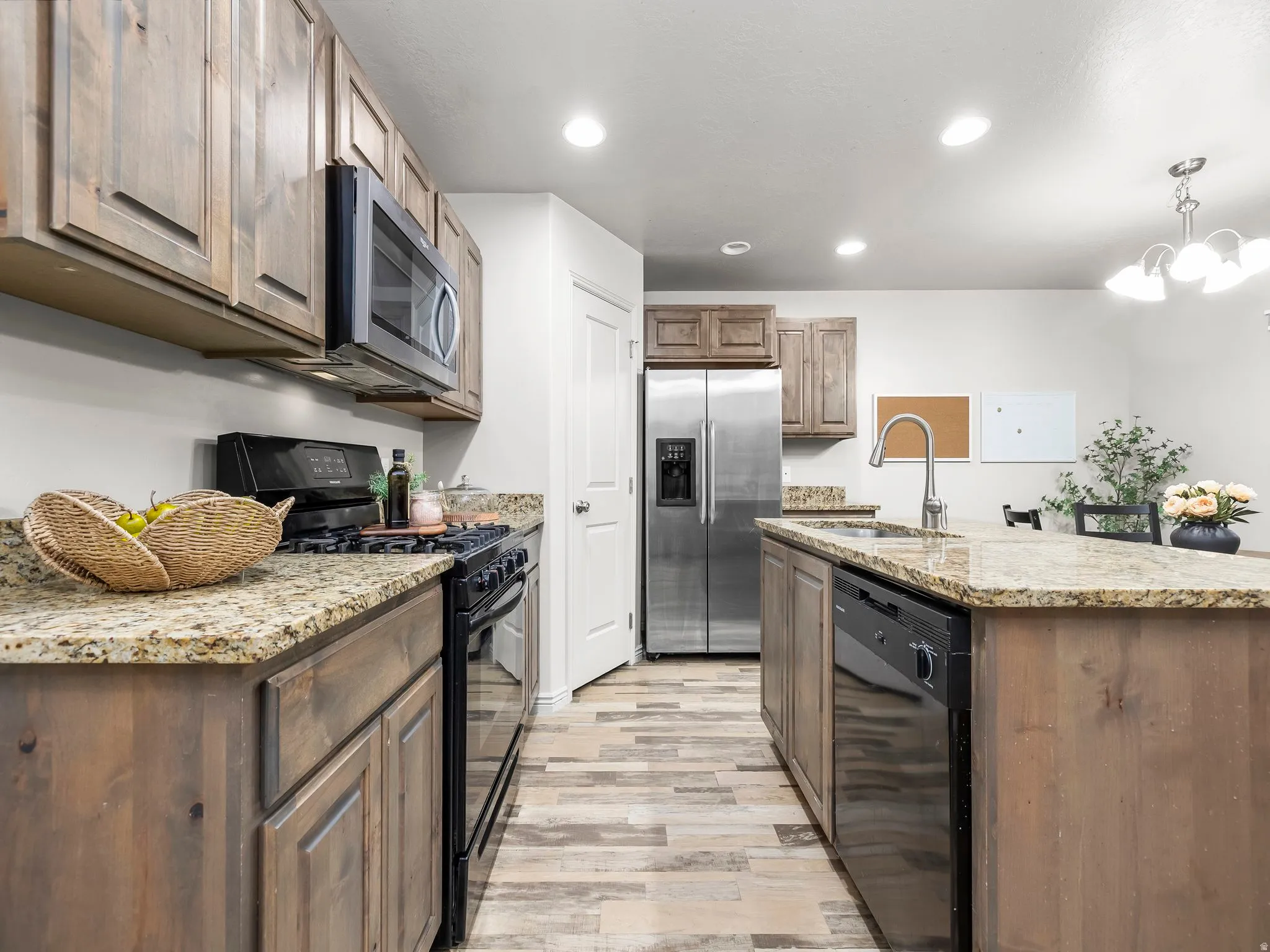 Kitchen with black appliances, a kitchen island with sink, light stone countertops, recessed lighting, and a chandelier