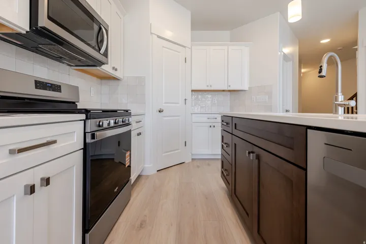 Kitchen with stainless steel appliances, two tone cabinetry, light wood-type flooring, decorative backsplash, and recessed lighting